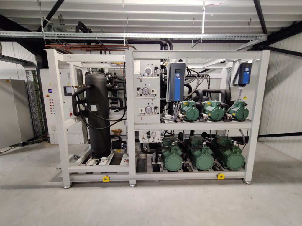 Industriële koelinstallatie met een schakelkast en compressoreenheid, geïnstalleerd in een technische ruimte met metalen dakconstructie.