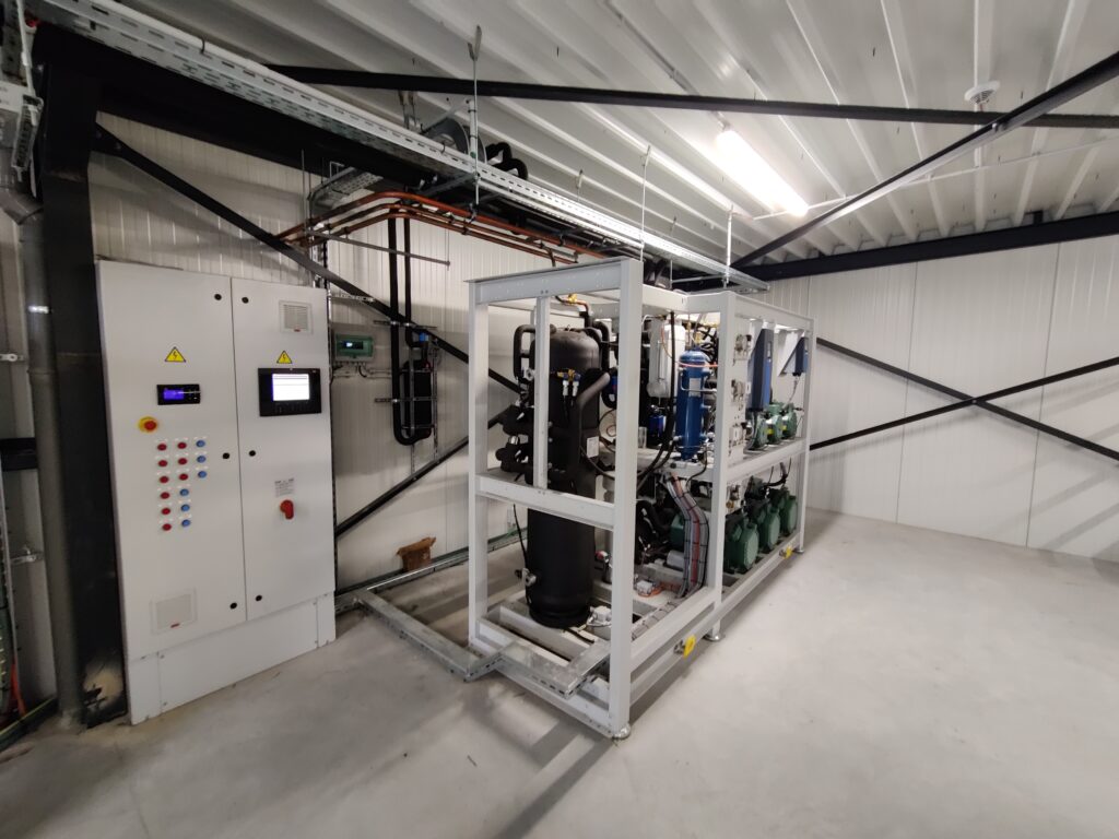 Industriële koelinstallatie met een schakelkast en compressoreenheid, geïnstalleerd in een technische ruimte met metalen dakconstructie.