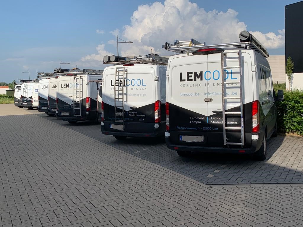 Een rij bedrijfswagens van Lemcool, specialist in koeltechniek, geparkeerd op een bedrijventerrein onder een blauwe lucht.